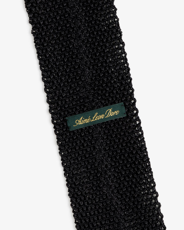 Crest Silk Knit Tie in black with a dark green fabric tag embroidered with gold text.