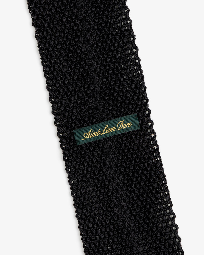 Crest Silk Knit Tie in black with a dark green fabric tag embroidered with gold text.