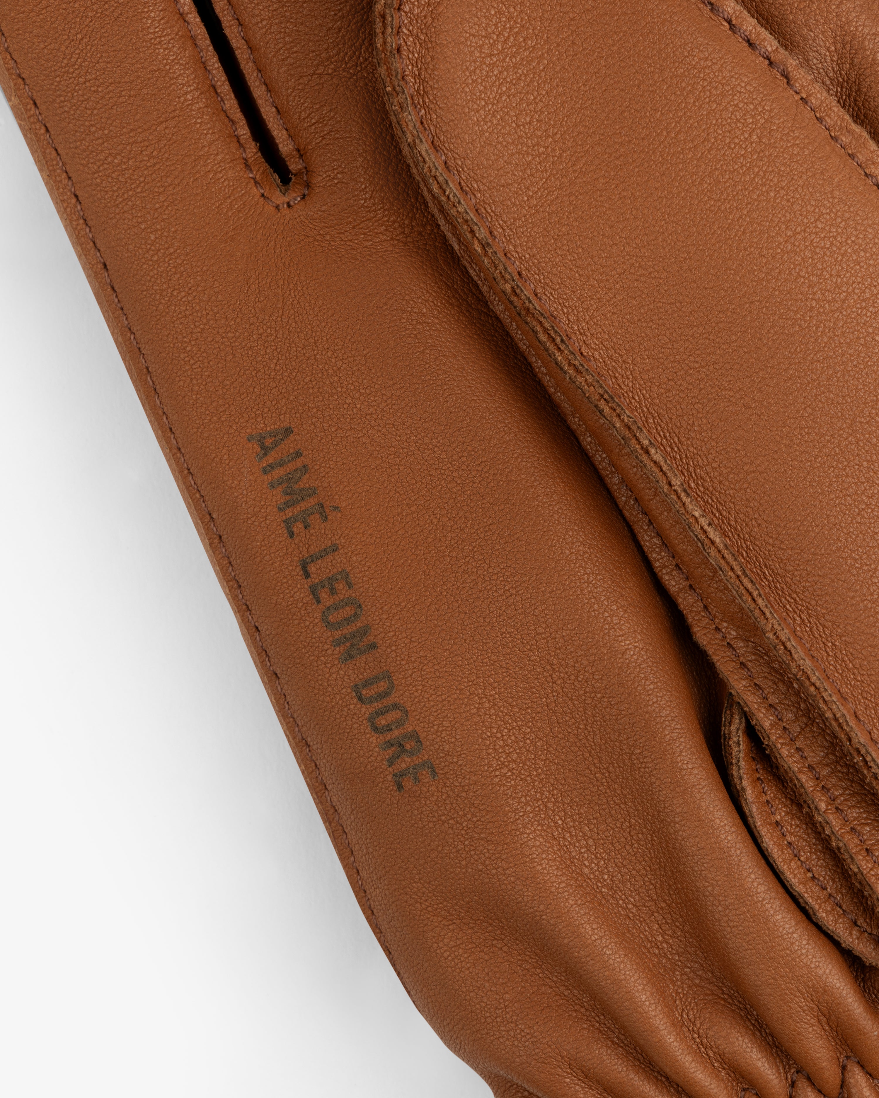 Close-up of brown leather Wakayama Gloves featuring the embossed text Aimé Leon Dore.