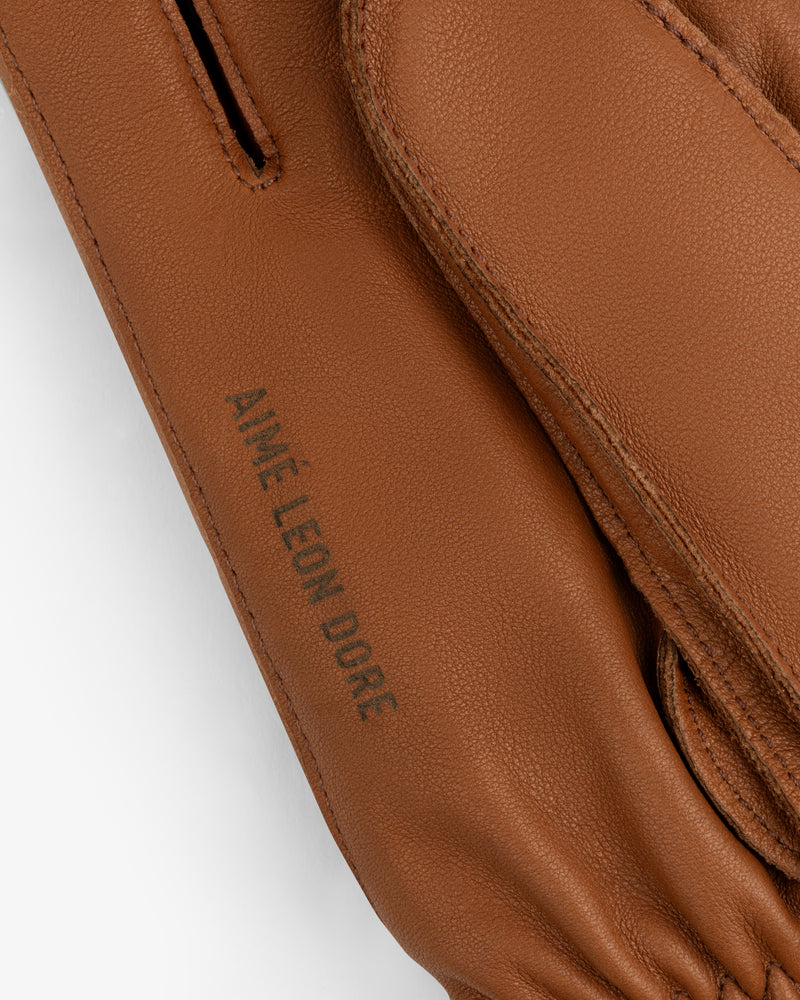 Close-up of brown leather Wakayama Gloves featuring the embossed text Aimé Leon Dore.