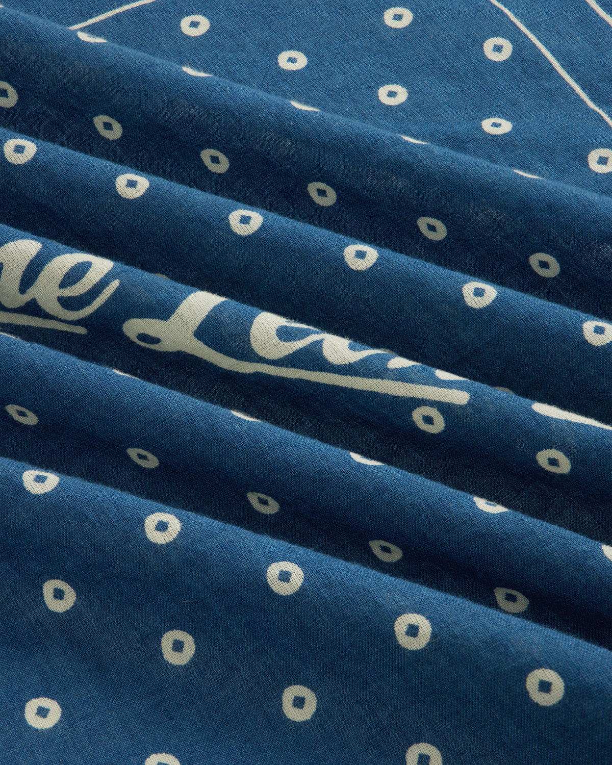 Indigo Dyed Cotton Bandana in blue with a white dot pattern and partial script text.
