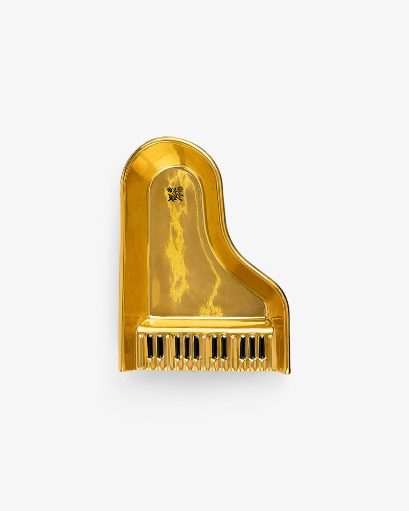 A shiny gold Piano Ashtray shaped like a grand piano, with raised black and white keys, against a white background.