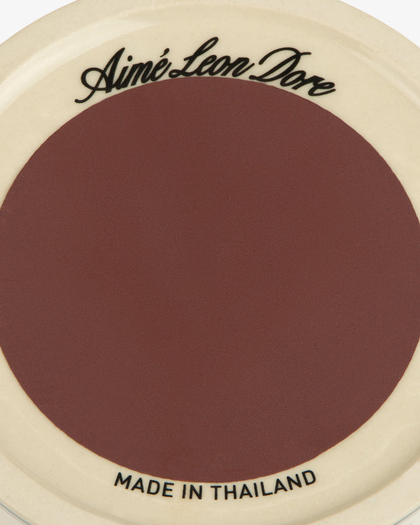 Porcelain Match Striker with Aimé Leon Dore text on top, Made in Thailand below. Brown center, cream border.