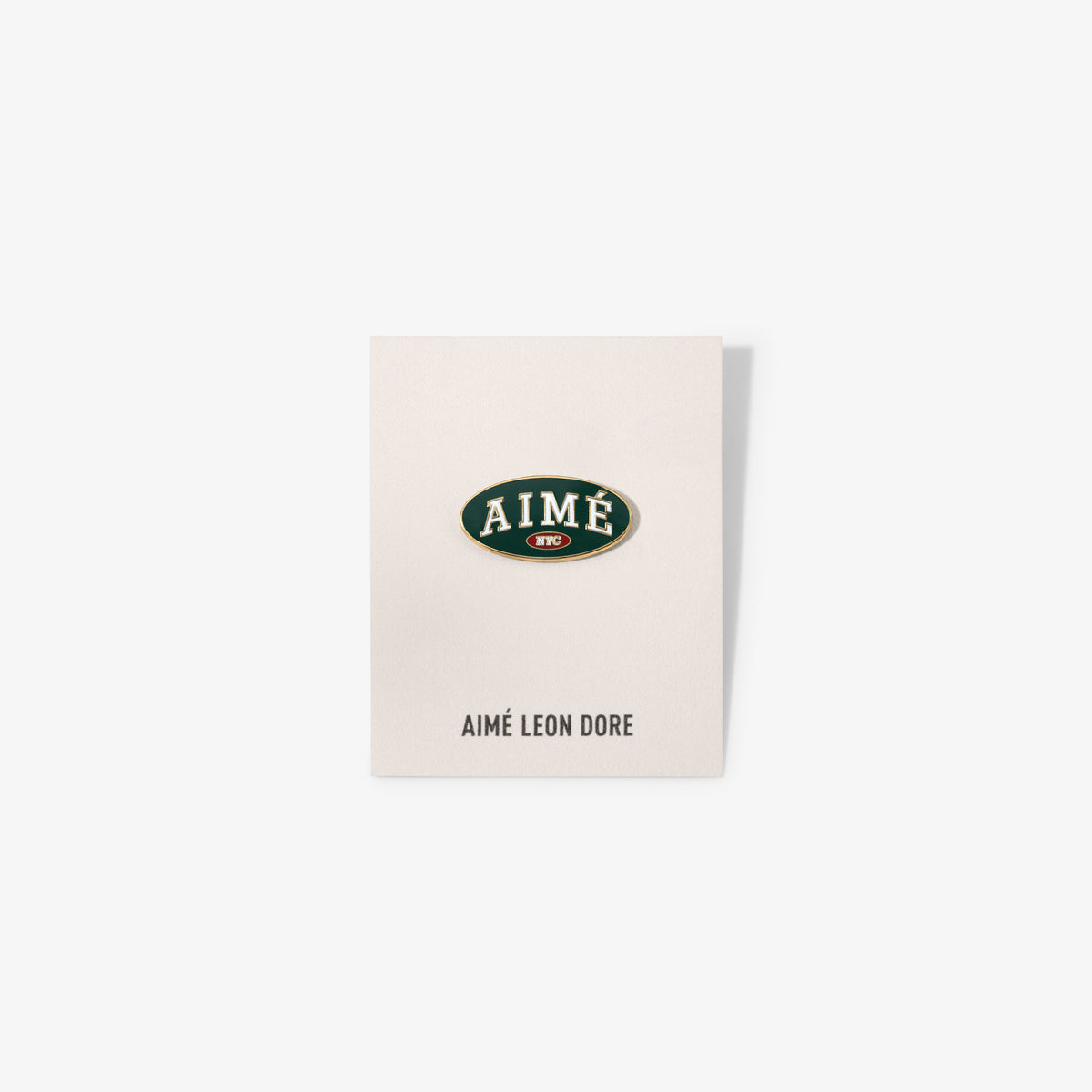Graphic Pin on a card with AIMÉ LEON DORE below, displayed against a plain white background.