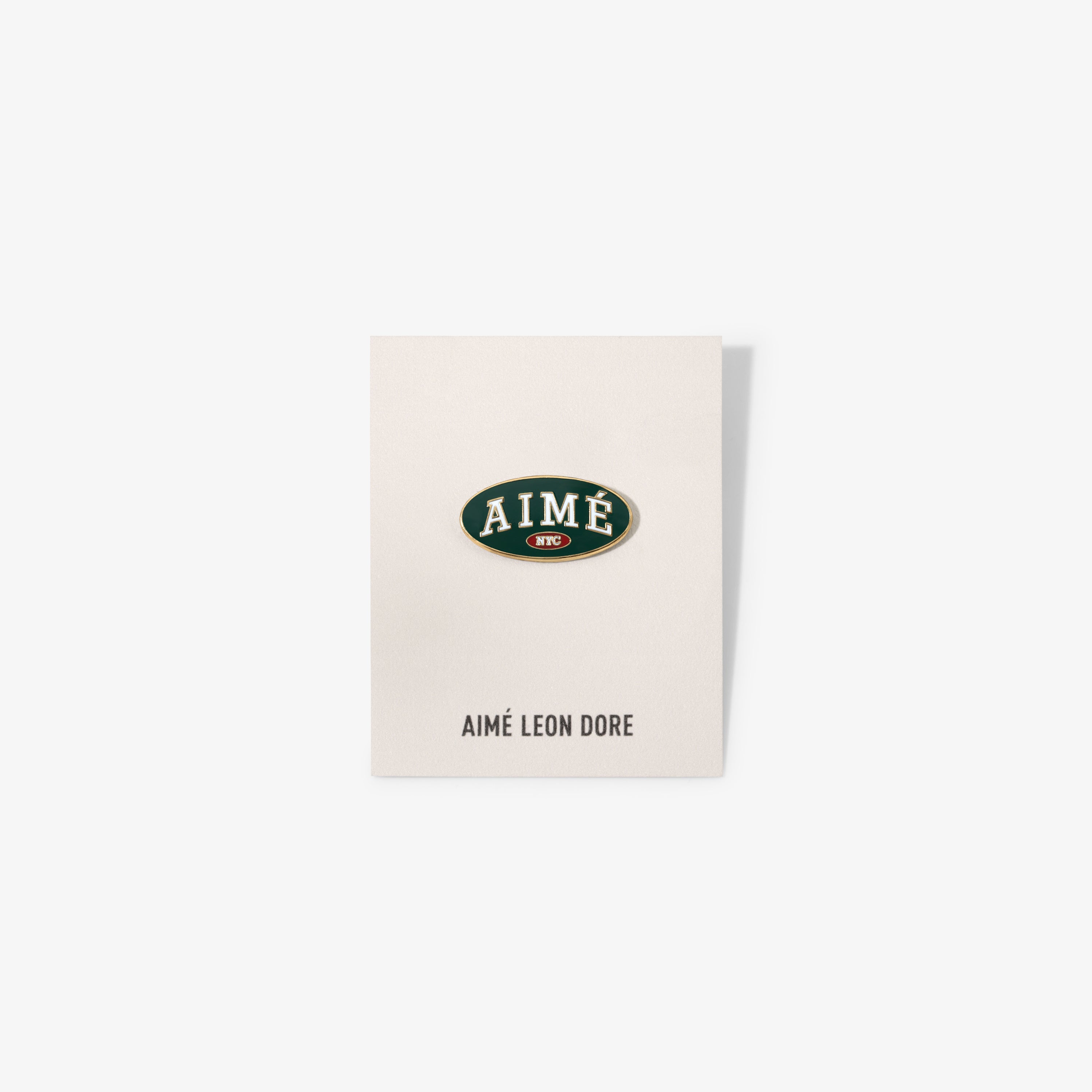 Graphic Pin on a card with AIMÉ LEON DORE below, displayed against a plain white background.
