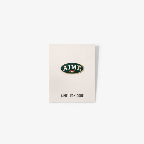 Graphic Pin on a card with AIMÉ LEON DORE below, displayed against a plain white background.