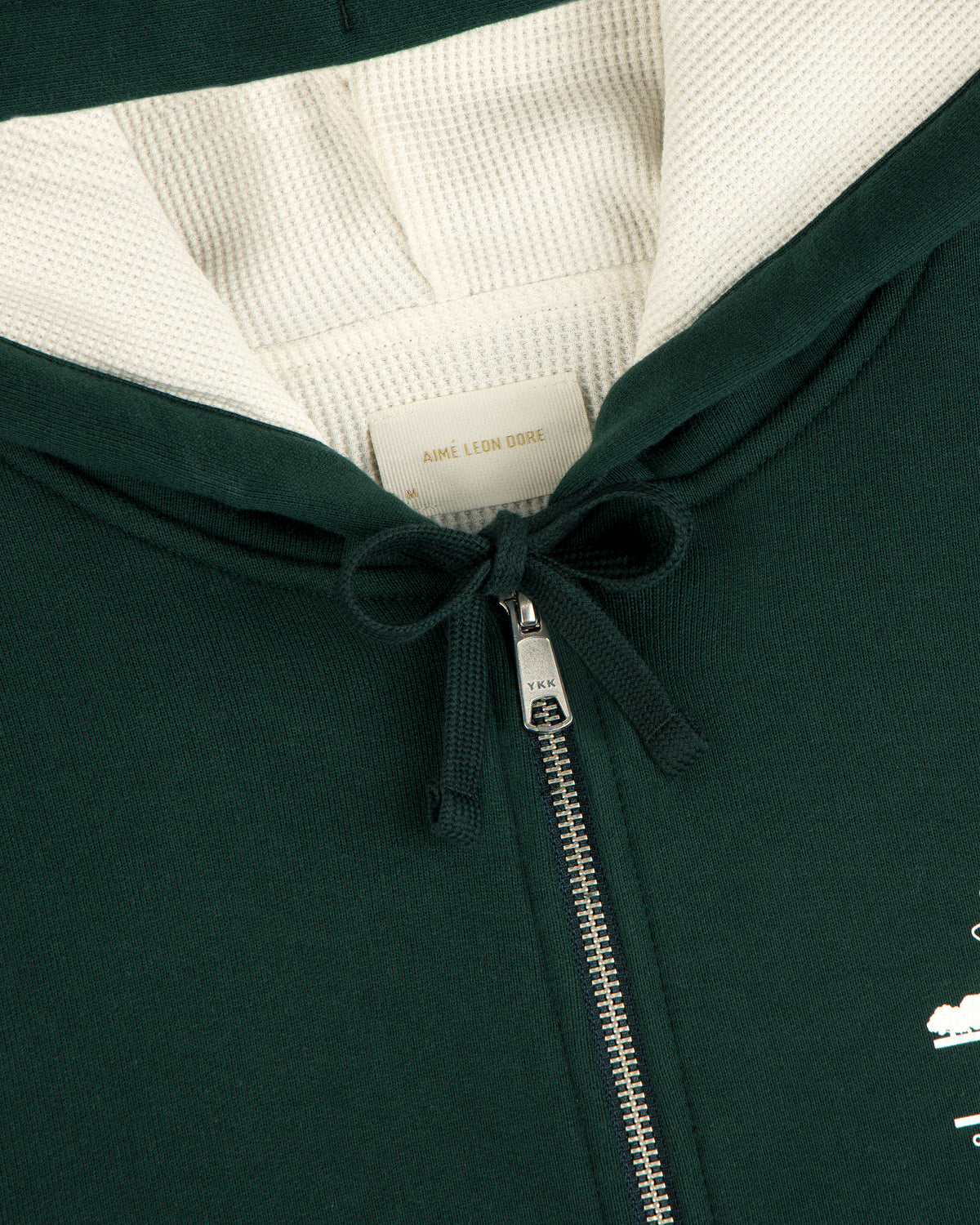 Close-up of the Unisphere Waffle Lined Full-Zip Hoodie in dark green, featuring a zipper, drawstrings, and inner label.