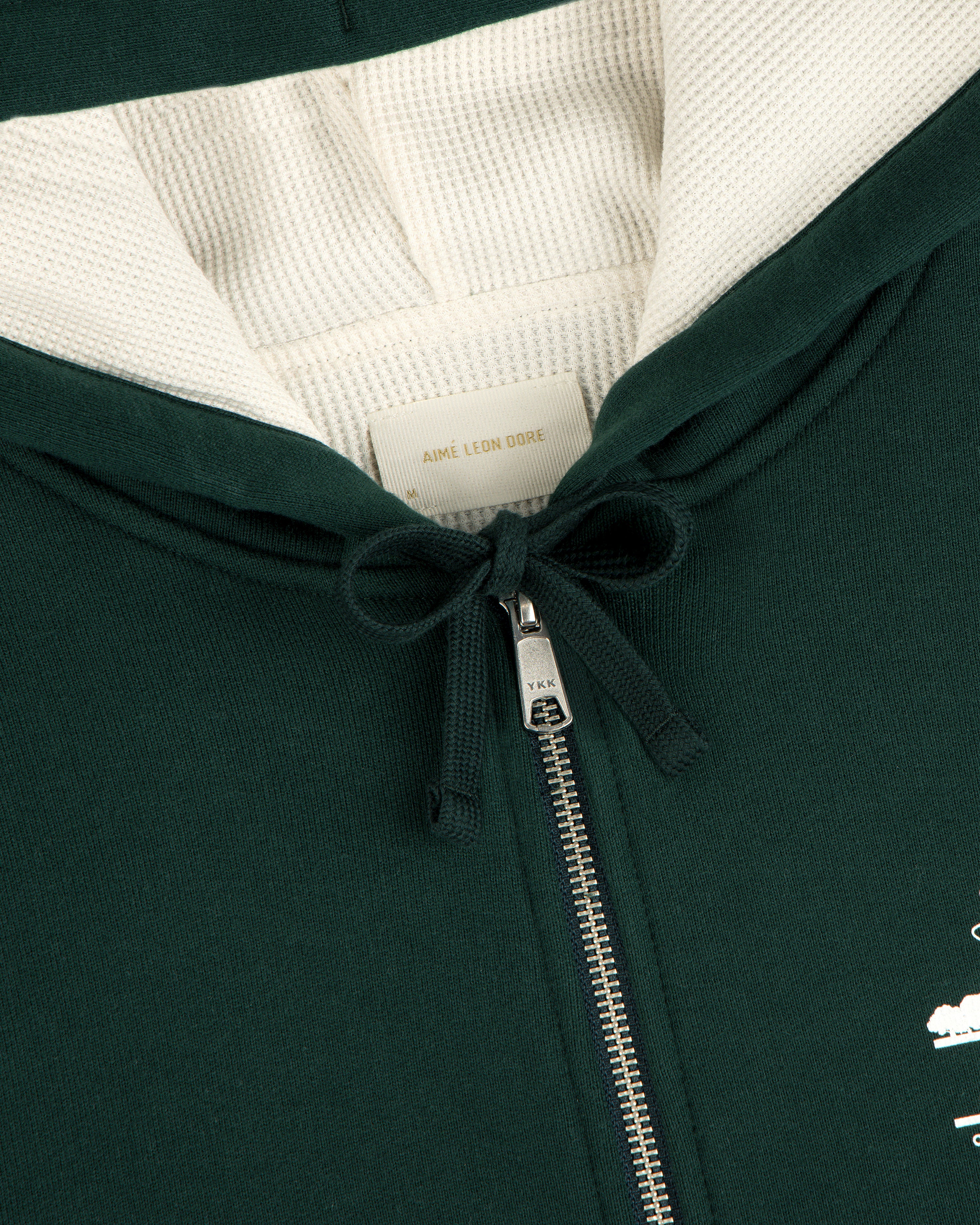 Close-up of the Unisphere Waffle Lined Full-Zip Hoodie in dark green, featuring a zipper, drawstrings, and inner label.