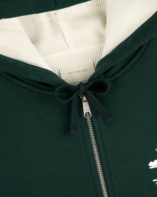 Close-up of the Unisphere Waffle Lined Full-Zip Hoodie in dark green, featuring a zipper, drawstrings, and inner label.
