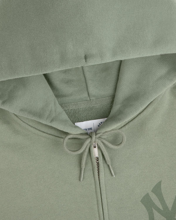 Close-up of a Yankees Washed Full-Zip Hoodie in sage green with a hood, zipper, and drawstring bow.