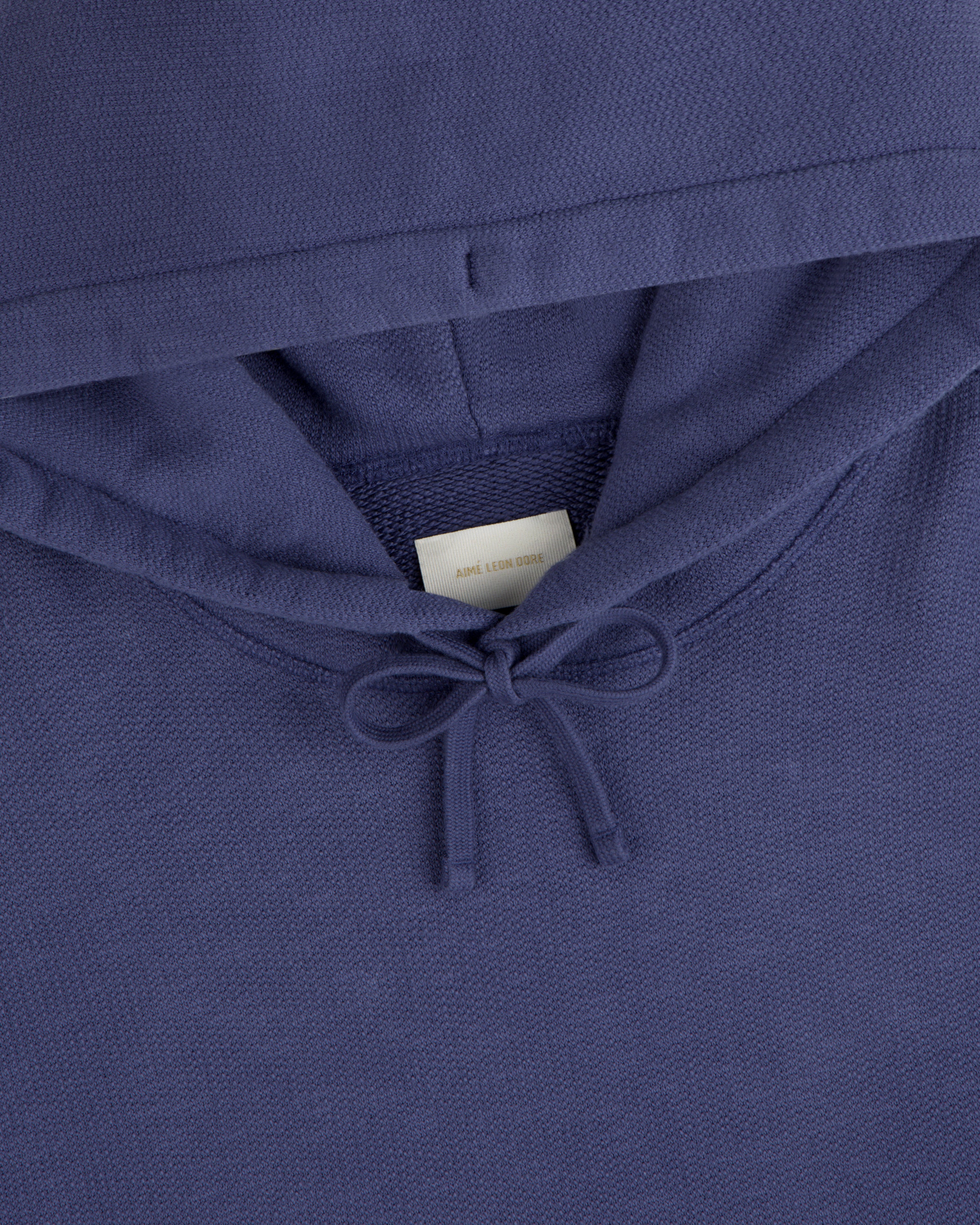 Close-up of the Stone Washed Marina Hoodie, blue with a bow-tied drawstring and a white label inside the collar.