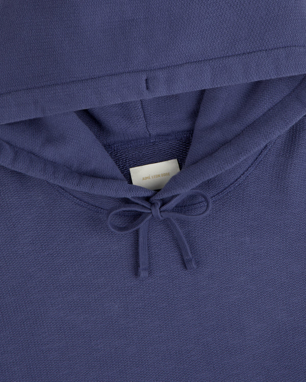 Close-up of the Stone Washed Marina Hoodie, blue with a bow-tied drawstring and a white label inside the collar.