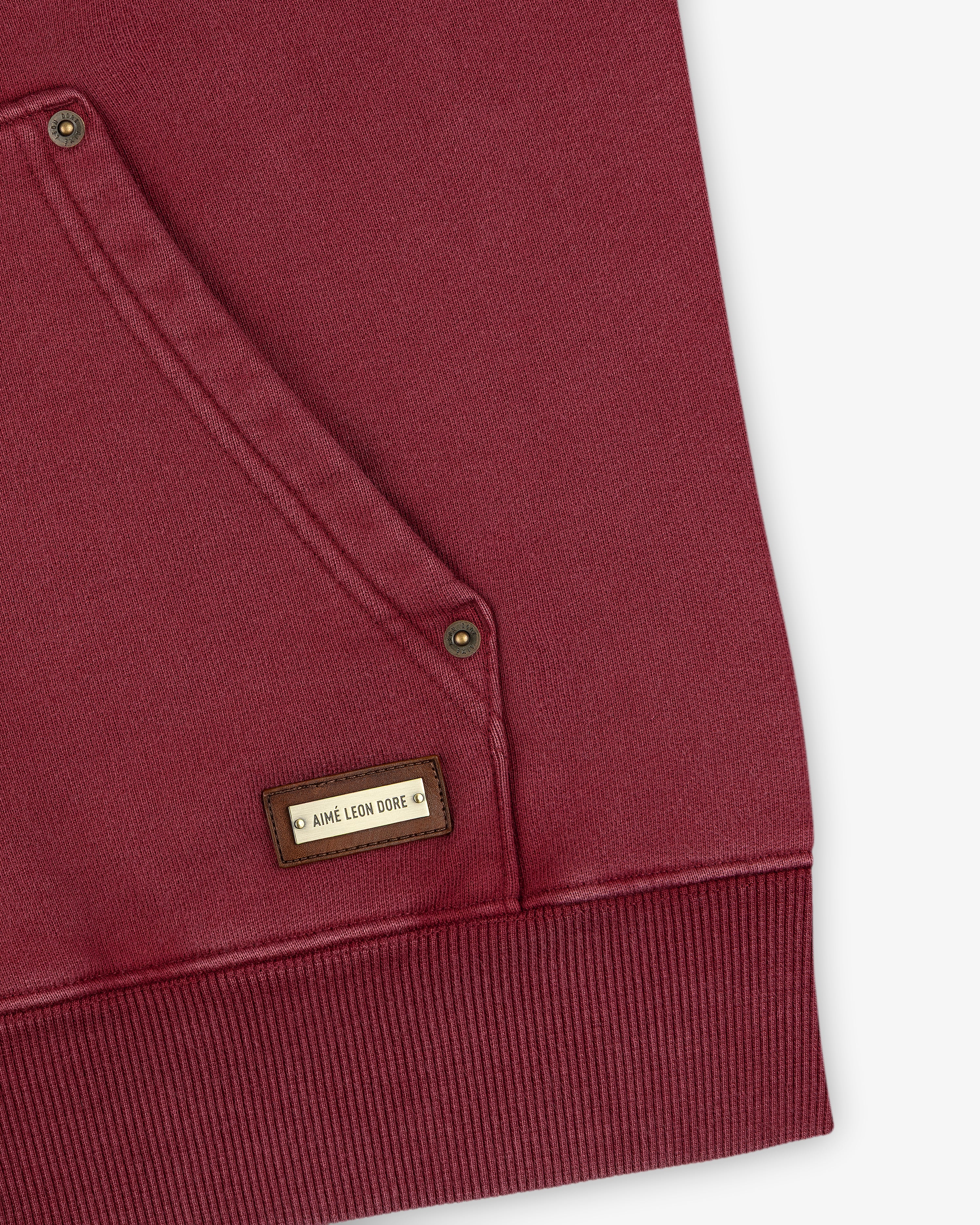 Close-up of a maroon Washed Full Zip Hoodie pocket with a small rectangular logo tag.