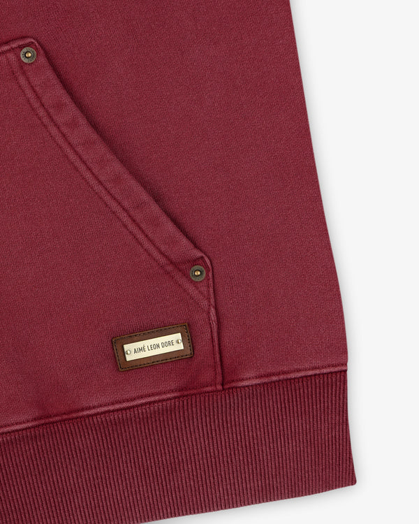 Close-up of a maroon Washed Full Zip Hoodie pocket with a small rectangular logo tag.