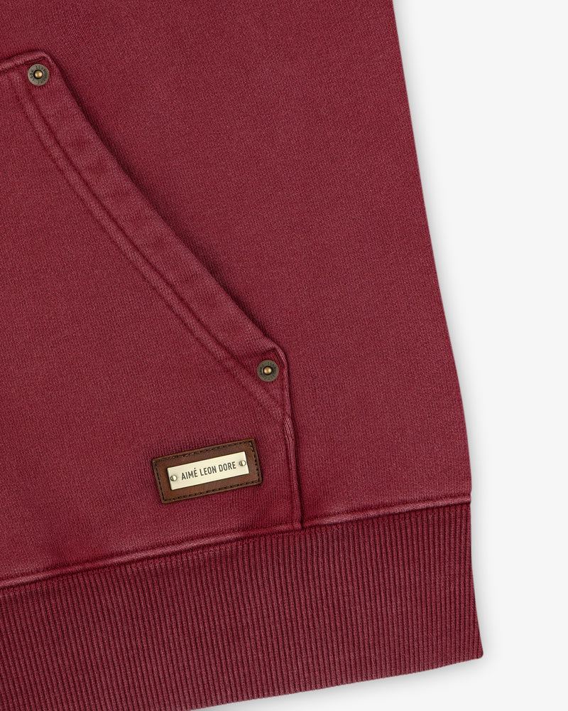 Close-up of a maroon Washed Full Zip Hoodie pocket with a small rectangular logo tag.