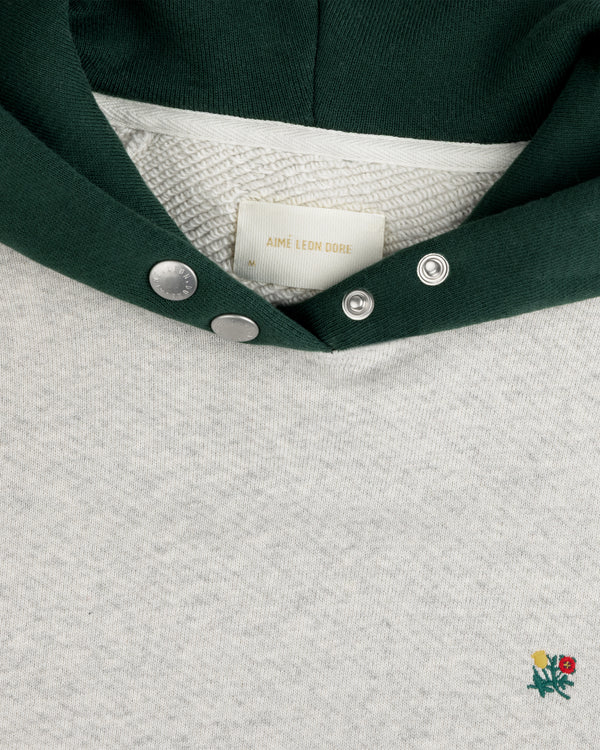Colorblock Crest Snap Hoodie in grey heather with a dark green hood, snap-button placket, and embroidered flower emblem.