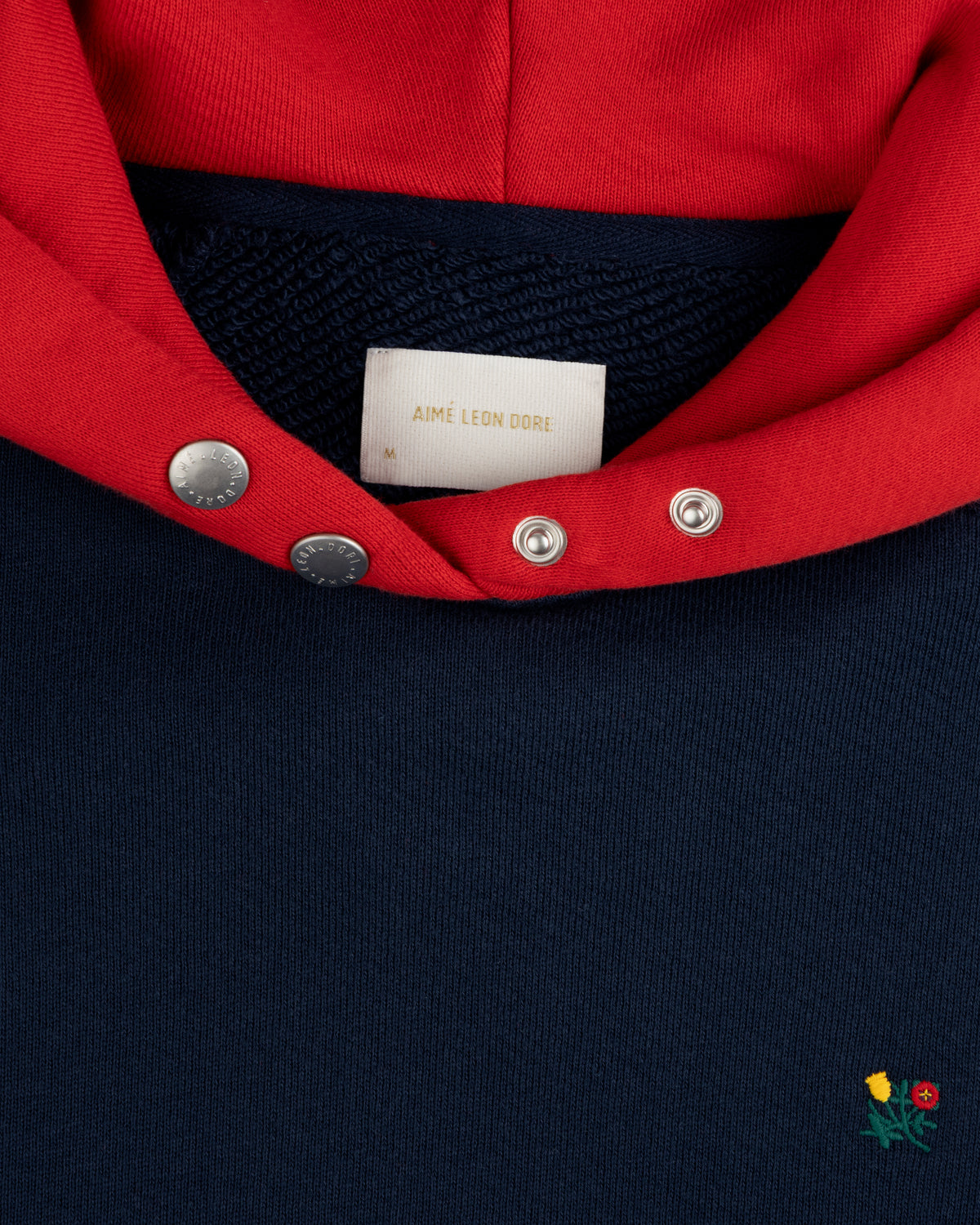 Colorblock Crest Snap Hoodie: navy blue with a red hood, snap-button placket, and small floral embroidery at the bottom.