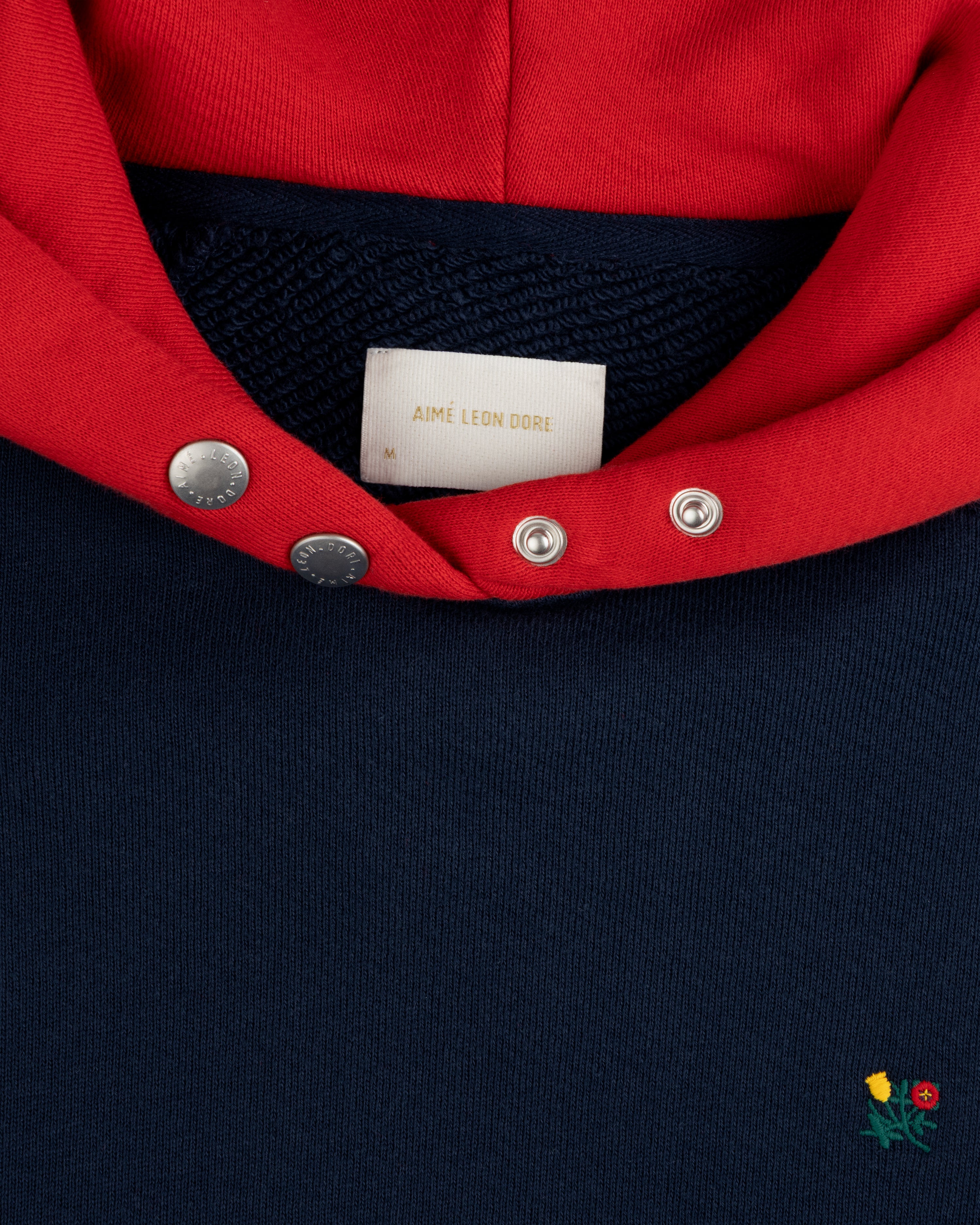 Colorblock Crest Snap Hoodie: navy blue with a red hood, snap-button placket, and small floral embroidery at the bottom.