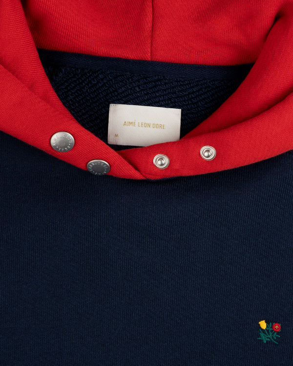 Colorblock Crest Snap Hoodie: navy blue with a red hood, snap-button placket, and small floral embroidery at the bottom.
