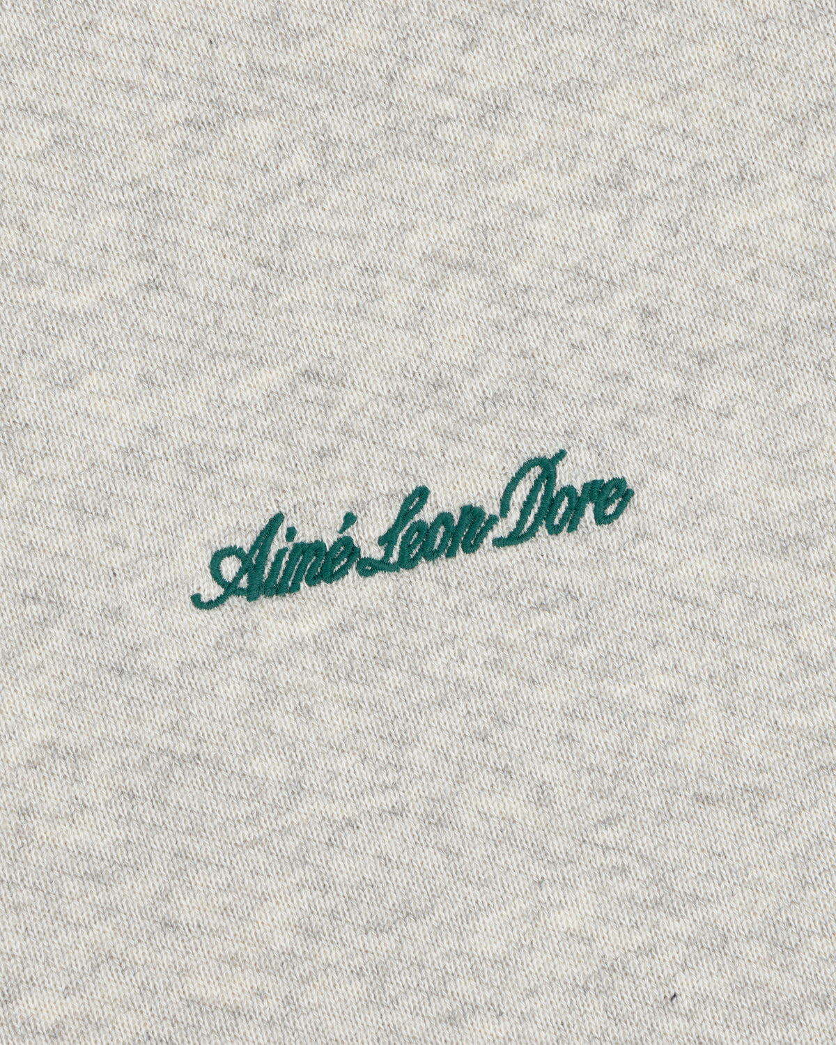 Dark green cursive Aimé Leon Dore embroidery on the grey heather fabric of a Script Full Zip Hoodie.