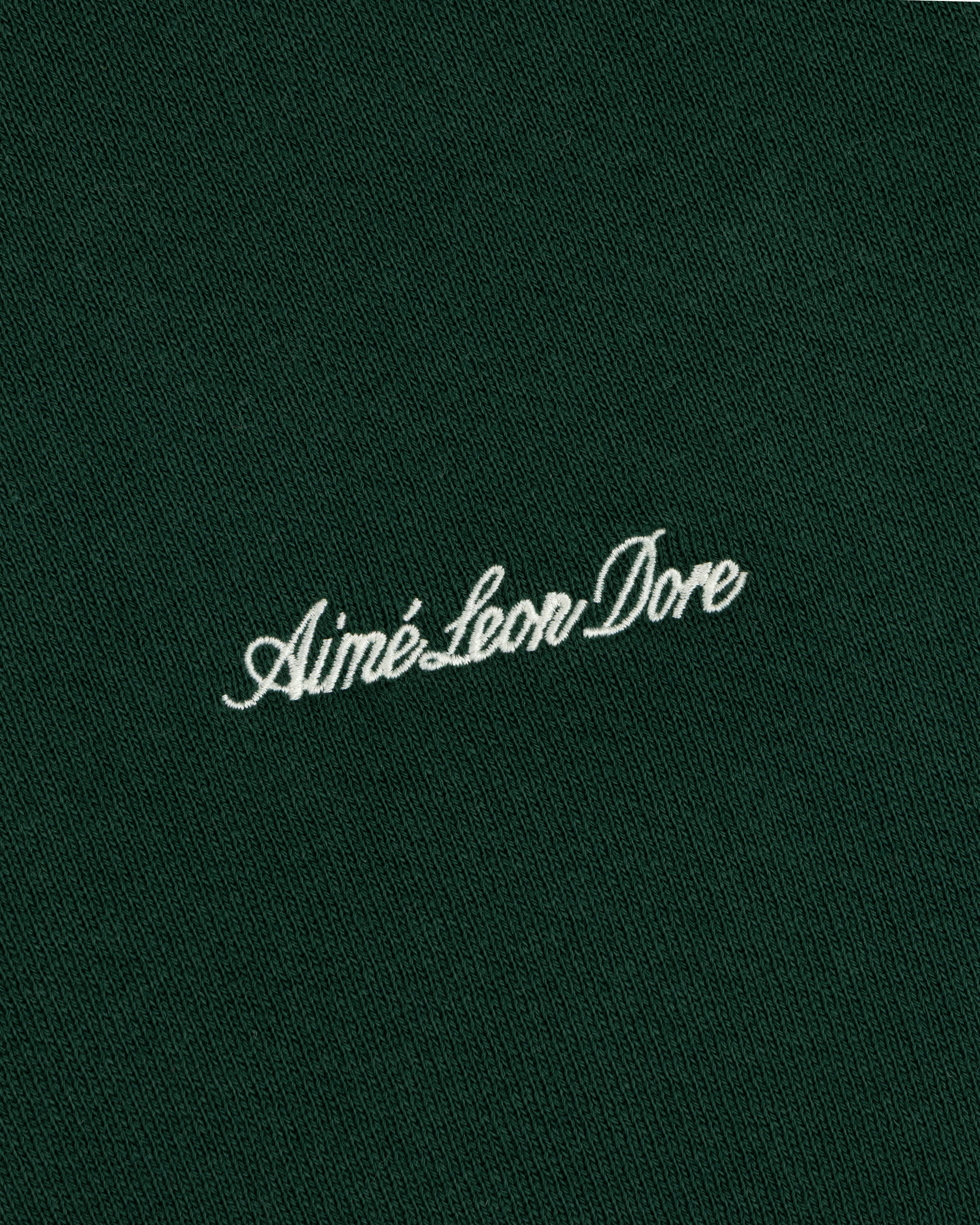White embroidered Script Full Zip Hoodie logo on a dark green fabric background.