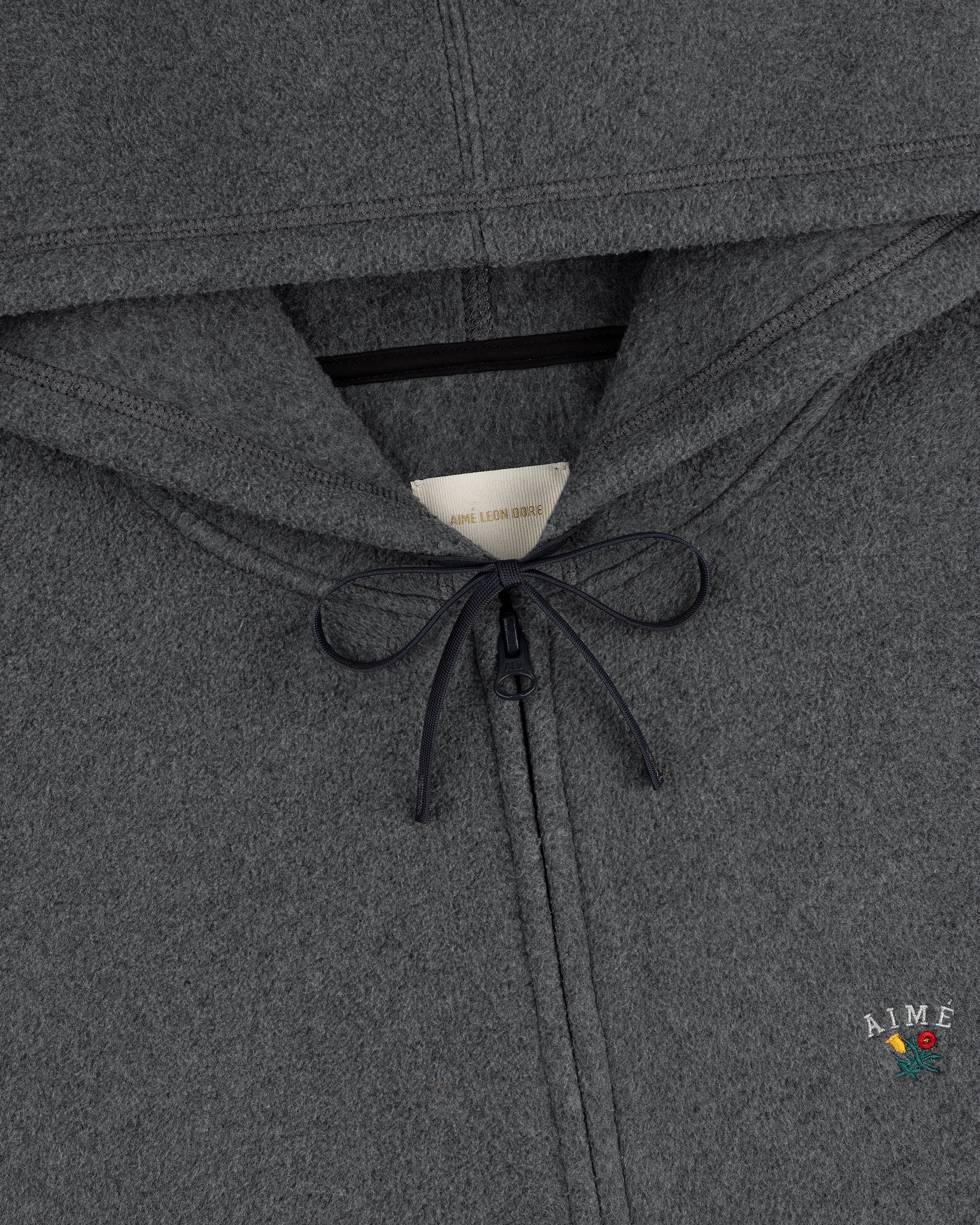 Close-up of Crest Fleece Full-Zip Hoodie in gray with a drawstring, zipper, and AIME embroidery accented by a red flower.