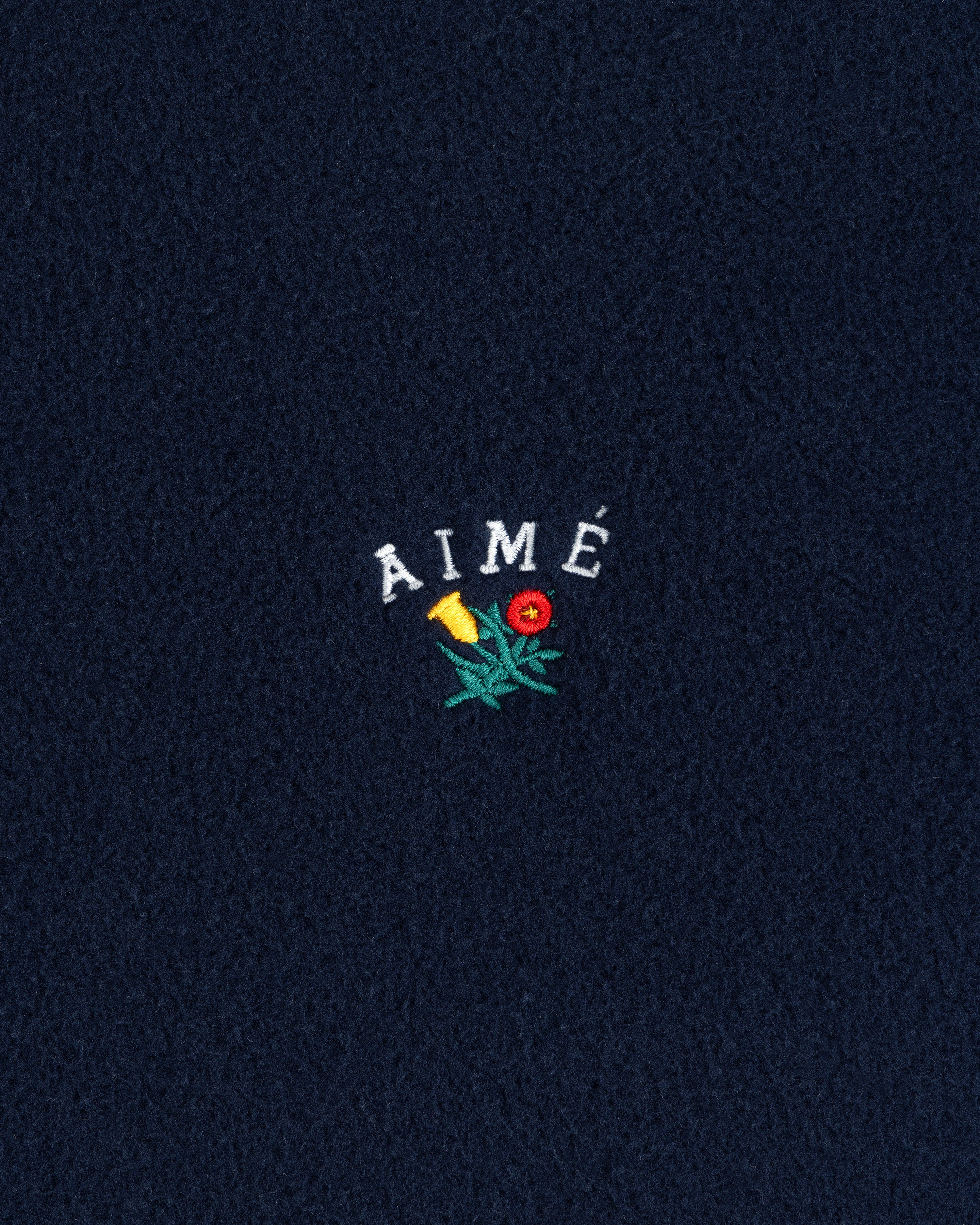 Navy Crest Fleece Full-Zip Hoodie with AIMÉ text and a small yellow-red embroidered flower with green leaves.