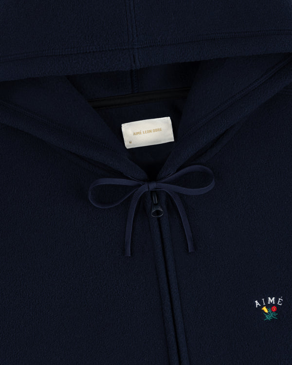 Detail of Crest Fleece Full-Zip Hoodie in navy with bow at neck and AIMÉ plus flower embroidered on chest.
