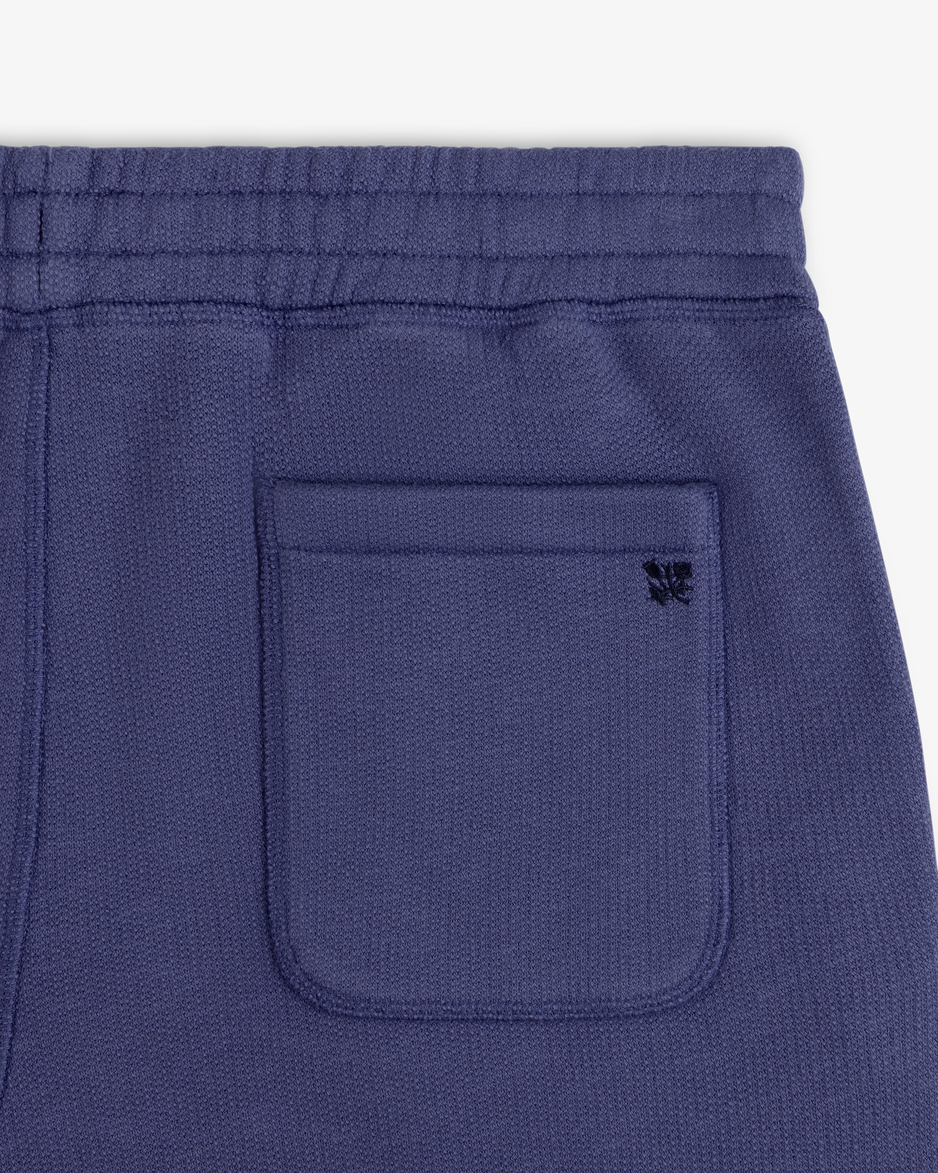 Close-up of Stone Washed Marina Sweatpants pocket with a small black embroidered butterfly on blue textured fabric.