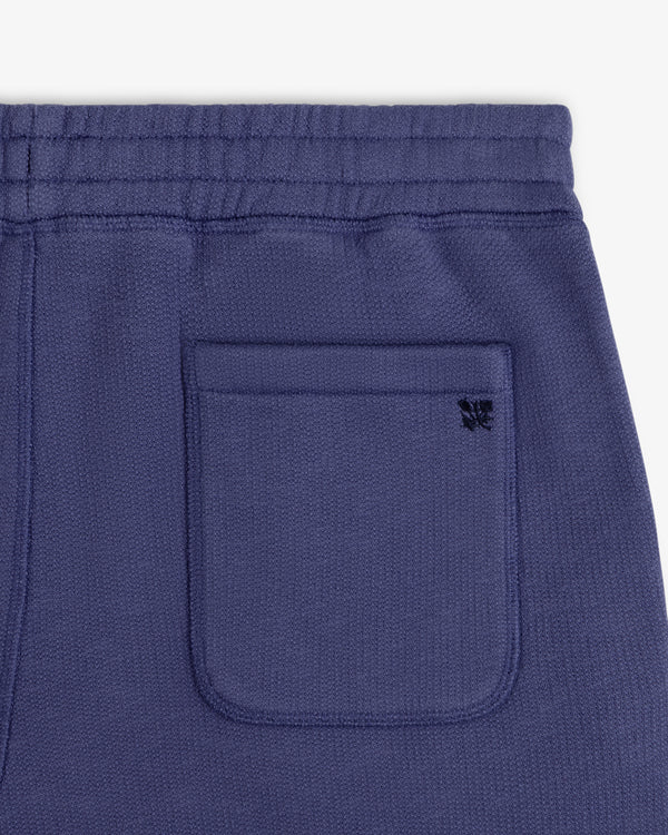 Close-up of Stone Washed Marina Sweatpants pocket with a small black embroidered butterfly on blue textured fabric.