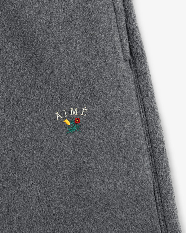 Close-up of gray Crest Fleece Sweatpant with AIMÉ and a small embroidered yellow and red flower detail.