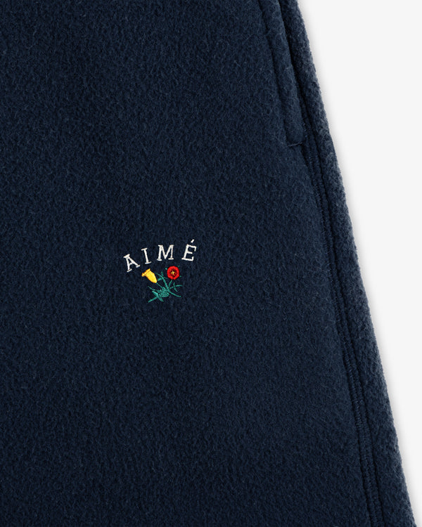 Close-up of Crest Fleece Sweatpant in navy with AIMÉ and small yellow and red embroidered flowers below the text.