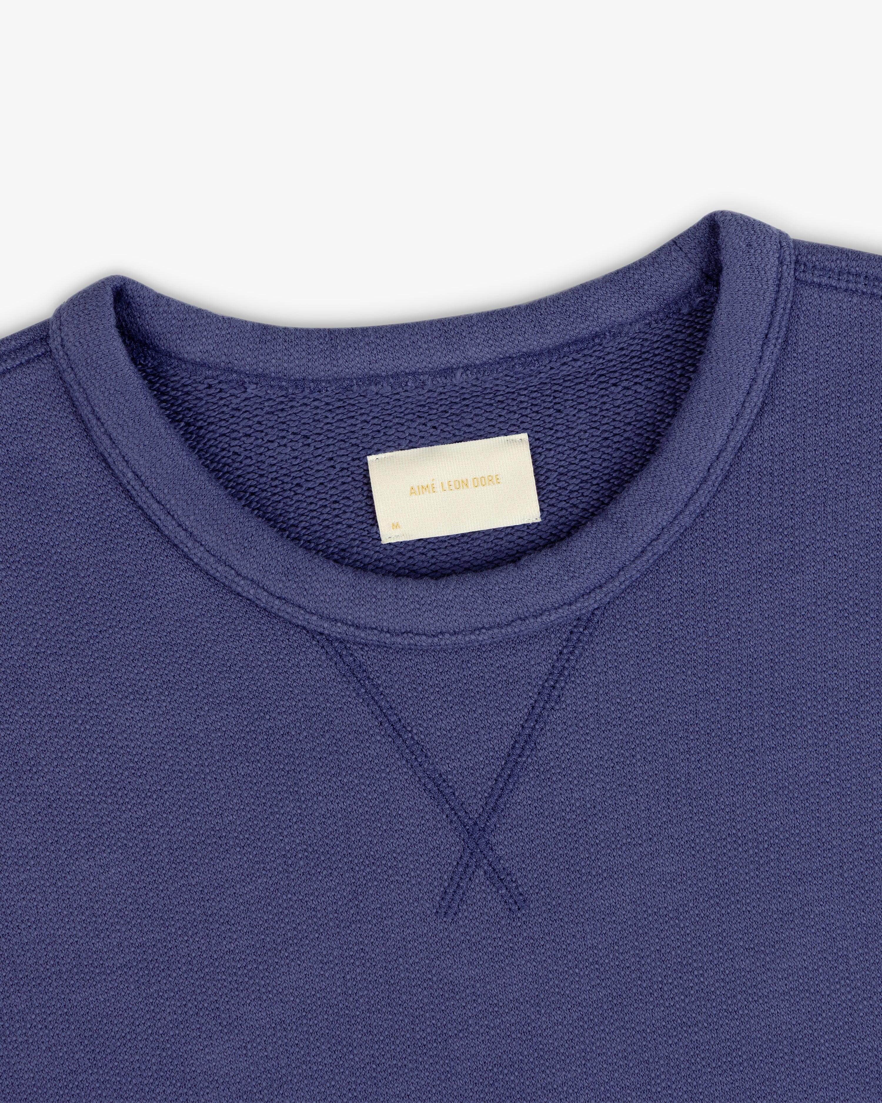Close-up of a Stone Washed Marina Crewneck Sweatshirt with a visible collar label reading Aime Leon Dore.