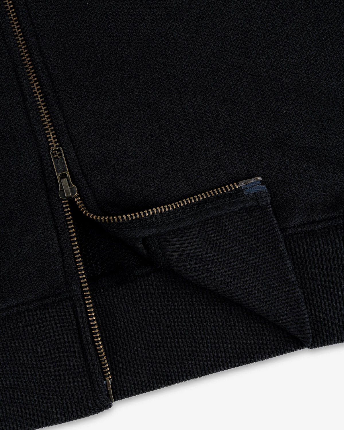 Close-up of Saint George Track Jacket hem with gold zipper partially unzipped, highlighting ribbed fabric details.