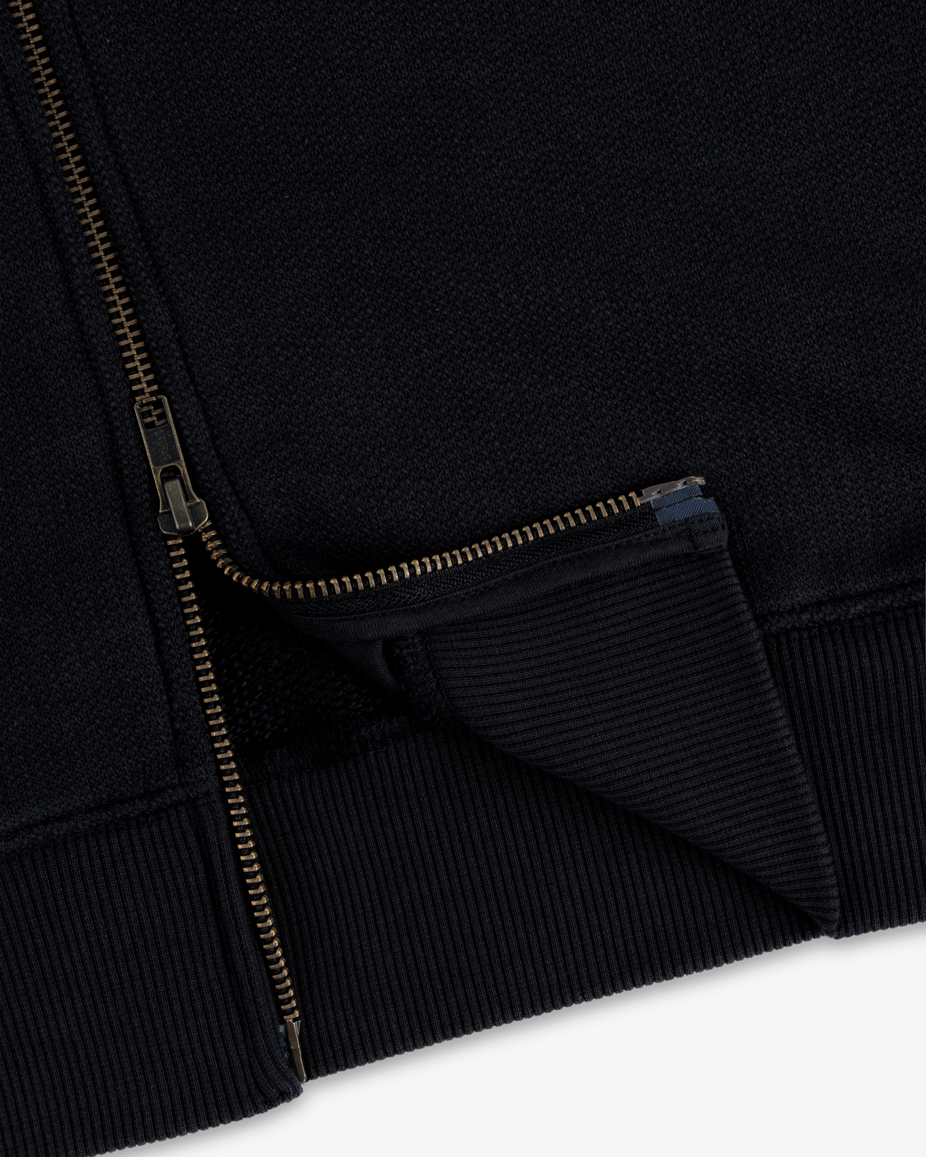 Close-up of Saint George Track Jacket hem with gold zipper partially unzipped, highlighting ribbed fabric details.