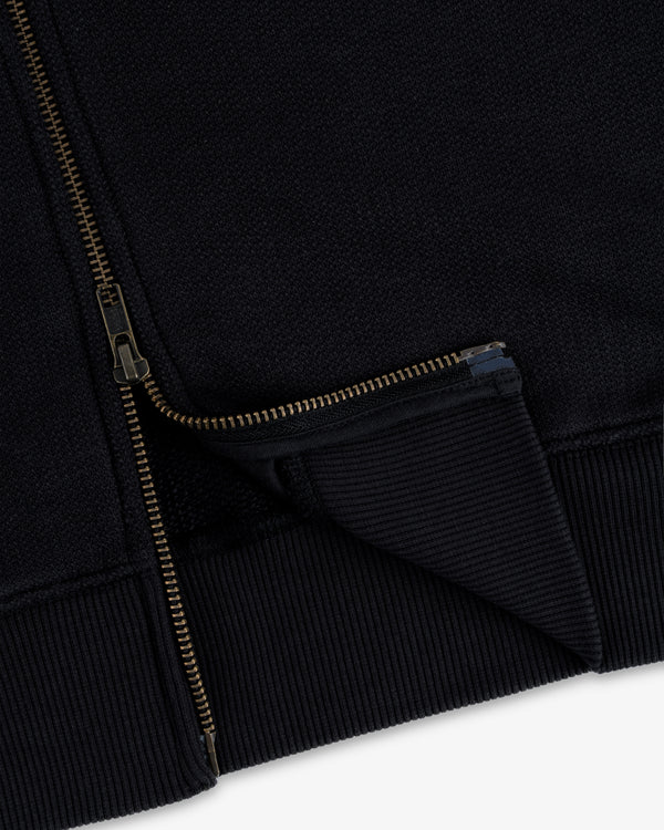 Close-up of Saint George Track Jacket hem with gold zipper partially unzipped, highlighting ribbed fabric details.