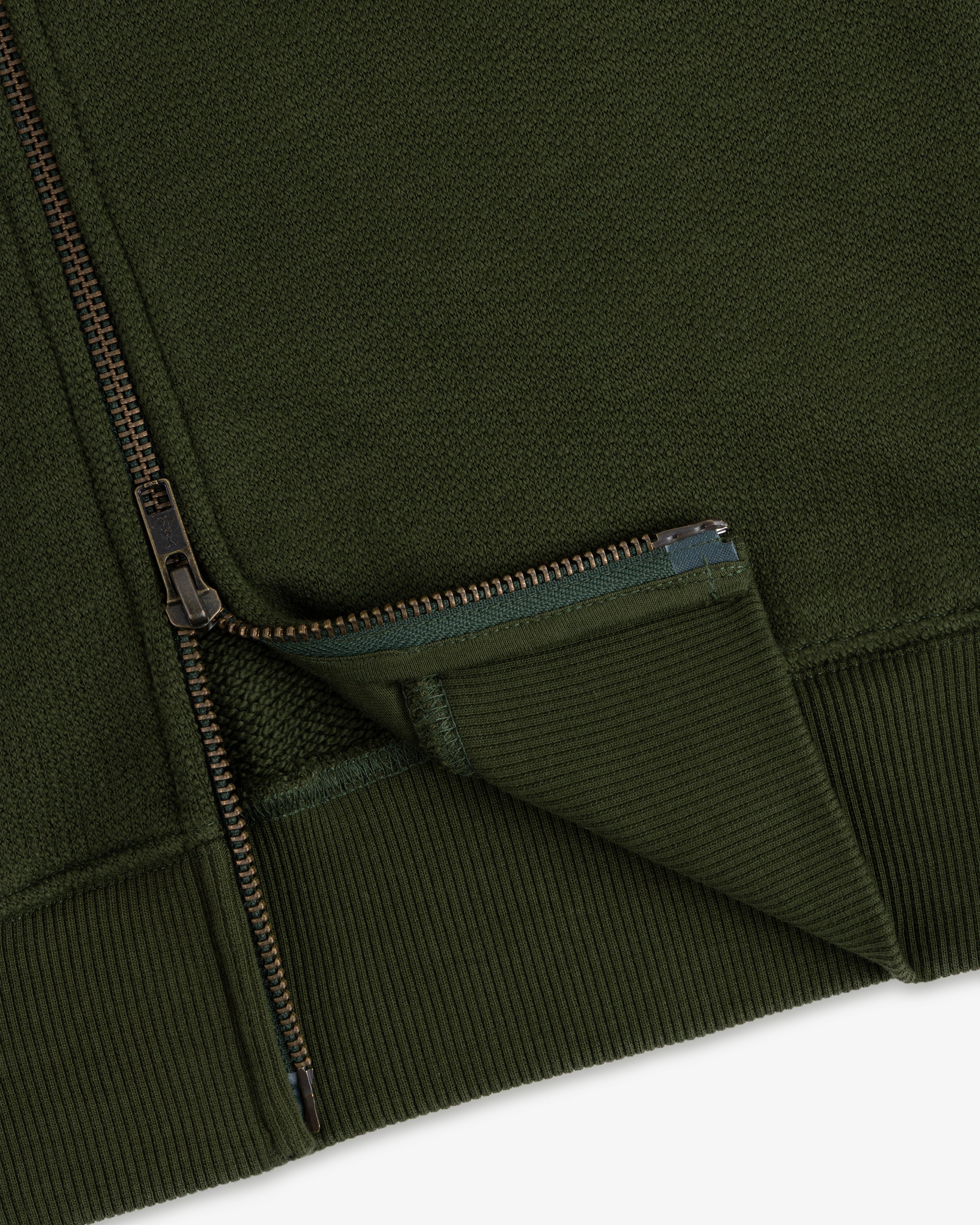 Close-up of the Saint George Track Jacket, featuring green fabric, a partially unzipped zipper, and ribbed edging.