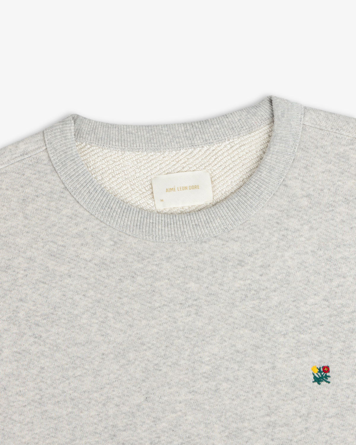 Grey Crest Crewneck Sweatshirt featuring a small embroidered floral detail and a brand label at the inner neckline.