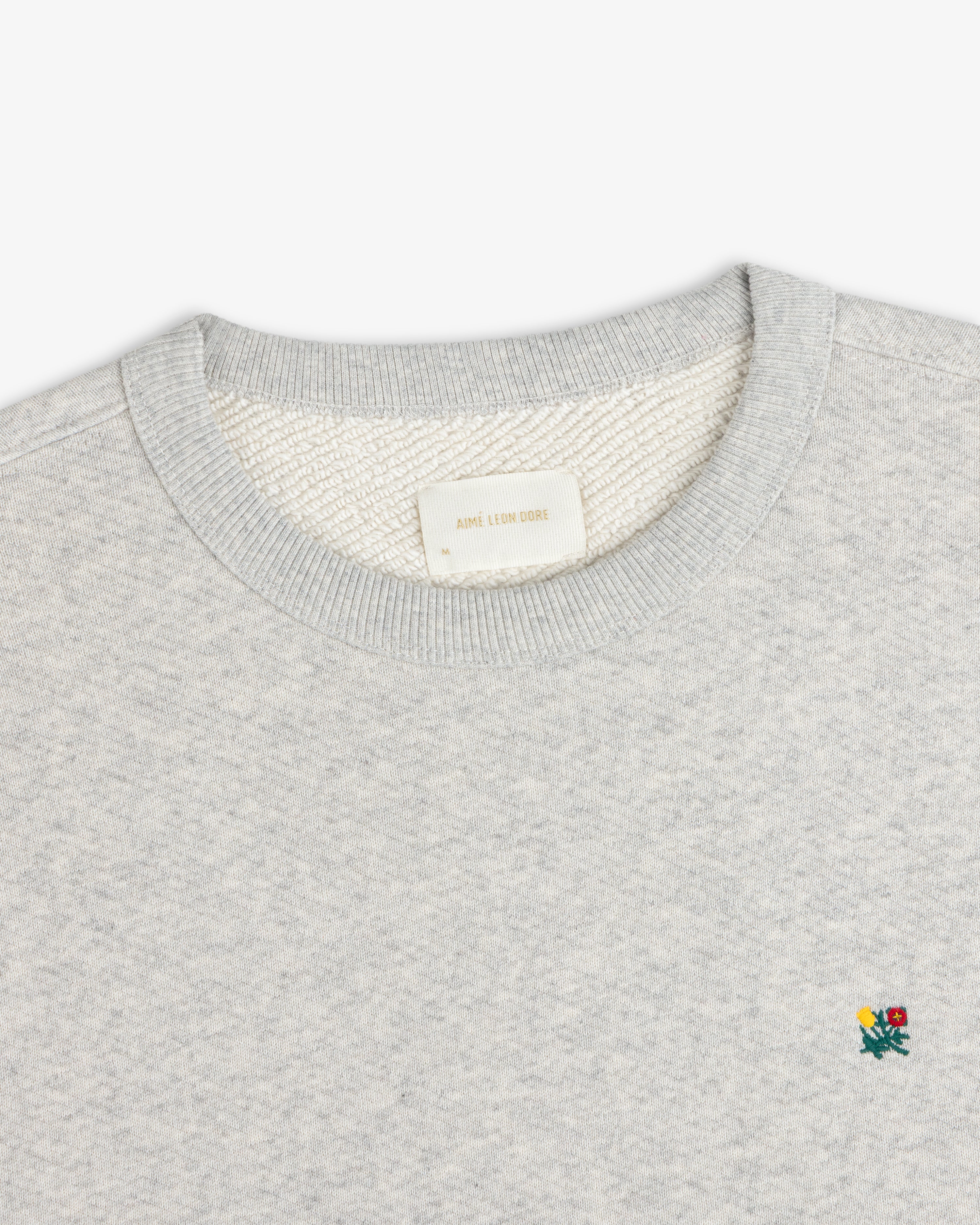 Grey Crest Crewneck Sweatshirt featuring a small embroidered floral detail and a brand label at the inner neckline.