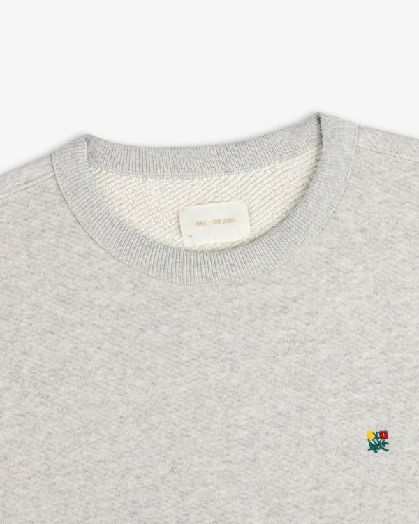 Grey Crest Crewneck Sweatshirt featuring a small embroidered floral detail and a brand label at the inner neckline.