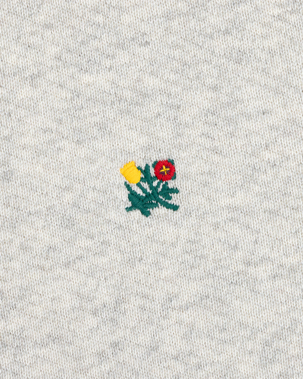 Crest Crewneck Sweatshirt with a small yellow and red flower patch embroidered on gray heathered fabric.
