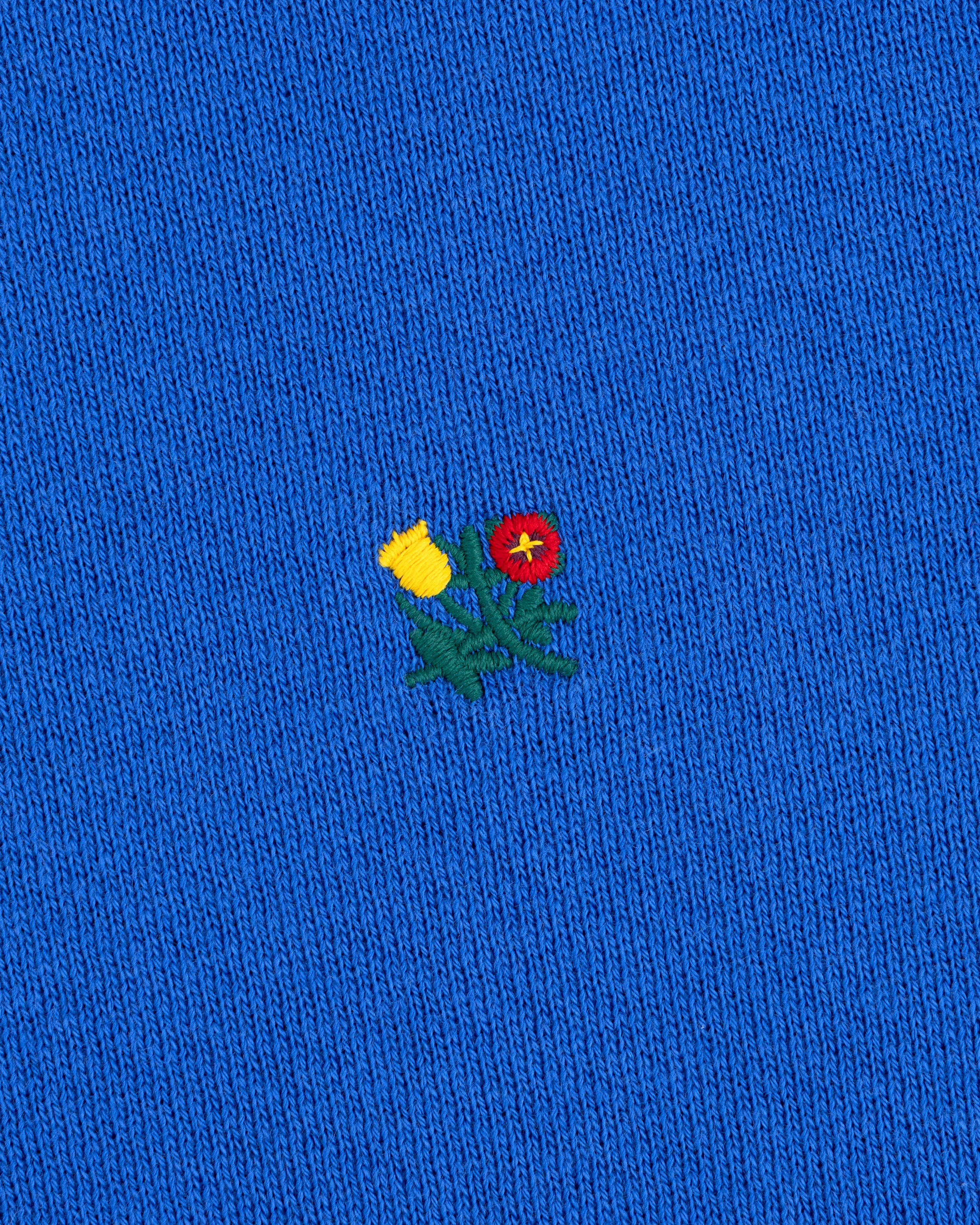 Crest Crewneck Sweatshirt in bright blue with a small embroidered yellow thistle and red flower.