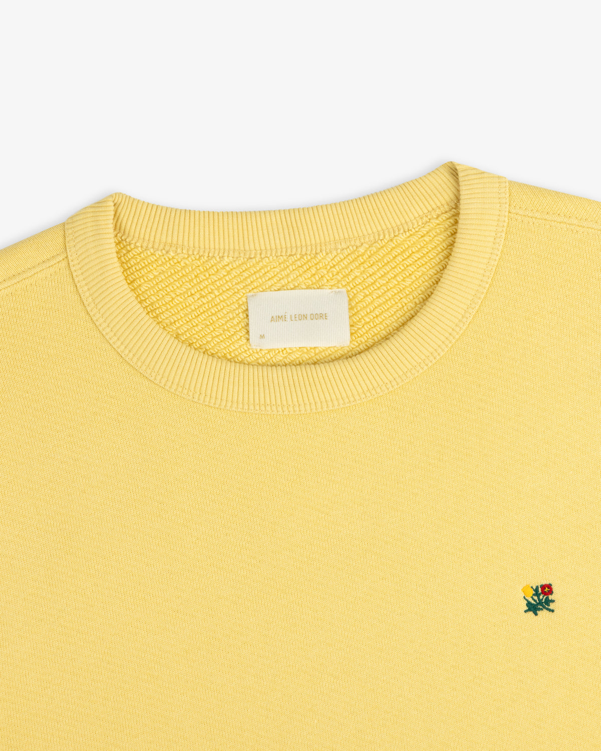 Pale yellow Crest Crewneck Sweatshirt featuring a small chest flower embroidery and a size M neck label.