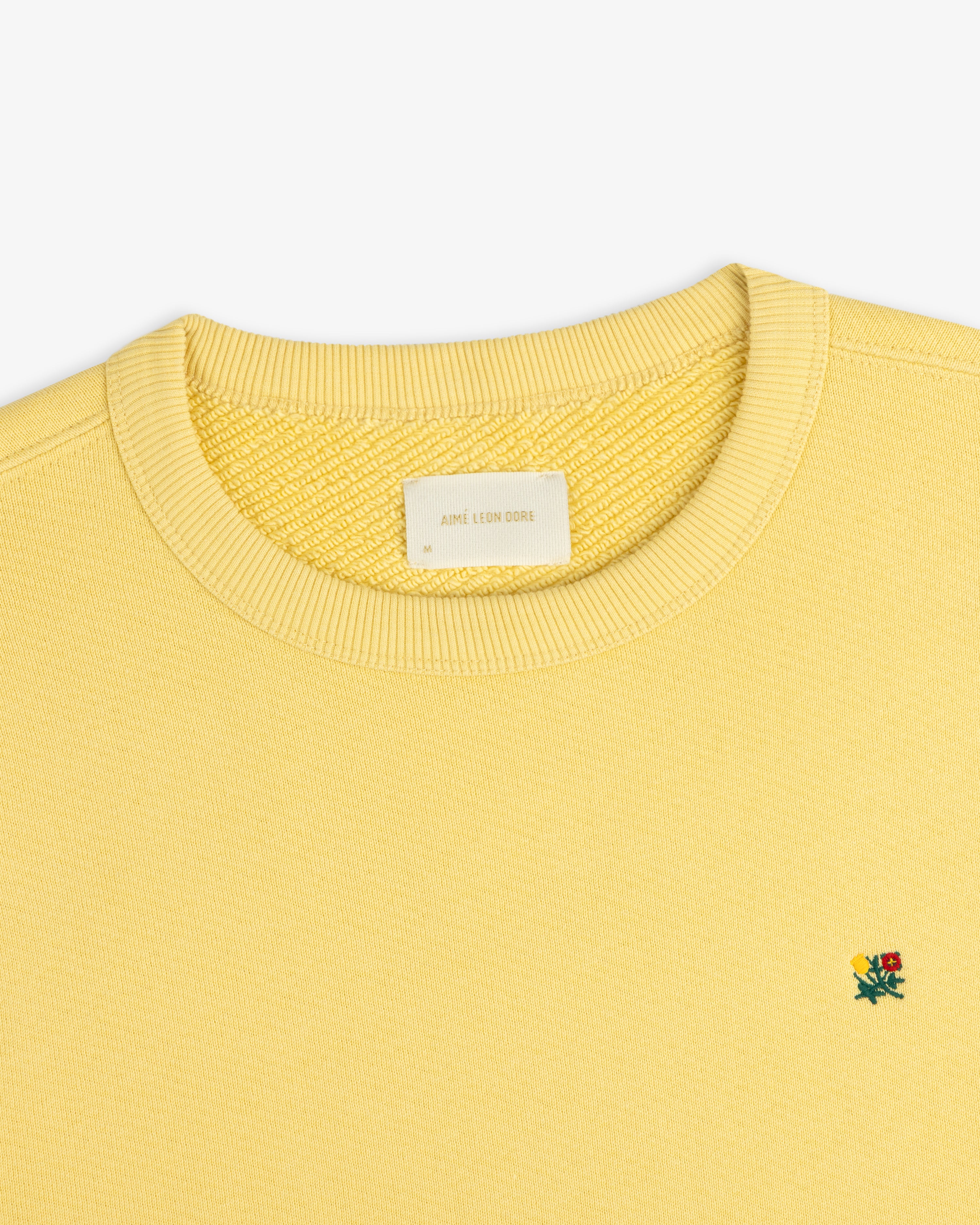 Pale yellow Crest Crewneck Sweatshirt featuring a small chest flower embroidery and a size M neck label.