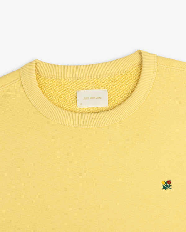 Pale yellow Crest Crewneck Sweatshirt featuring a small chest flower embroidery and a size M neck label.