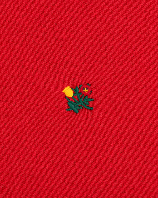 Crest Crewneck Sweatshirt in red with a small embroidered yellow thistle flower and green leaves.