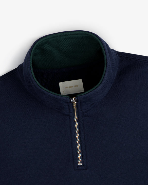 Aimé Souvenir Quarter Zip in navy with a silver zipper and dark green inner collar, shown on a white background.