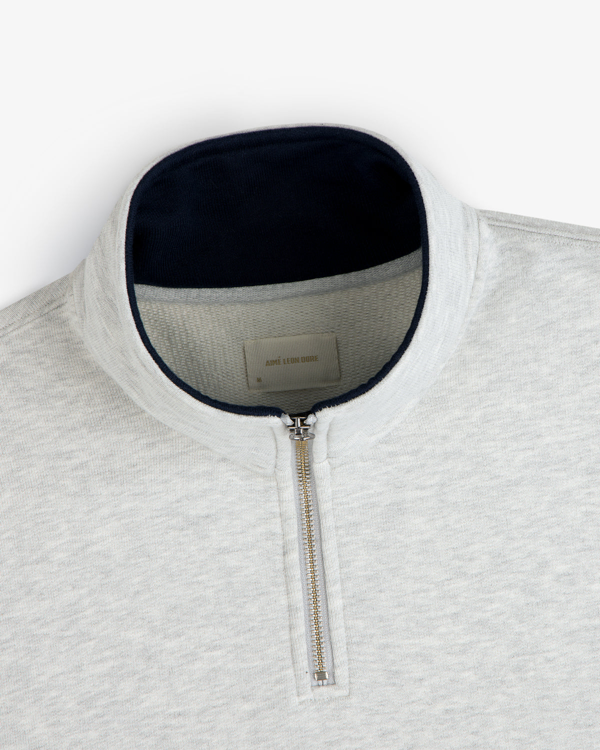 Aimé Souvenir Quarter Zip in light grey with silver zipper and dark collar lining, laid flat on a white background.