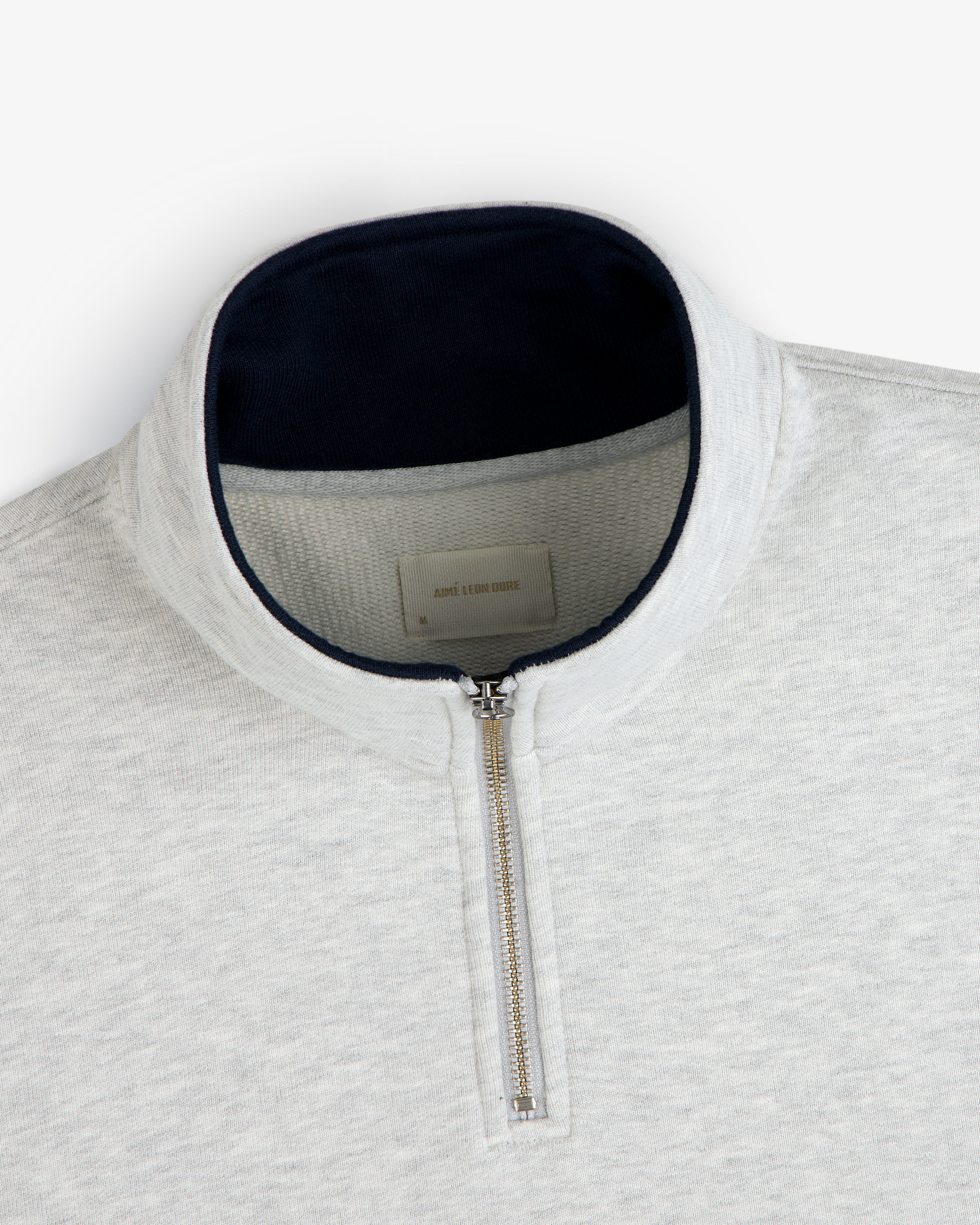 Aimé Souvenir Quarter Zip in light grey with silver zipper and dark collar lining, laid flat on a white background.