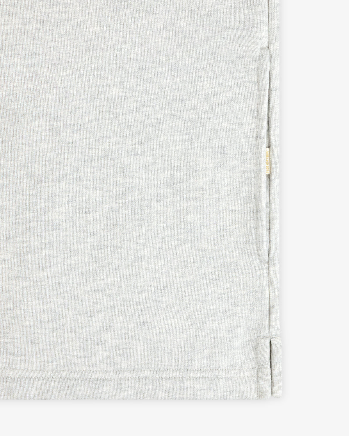 Close-up of the Aimé Souvenir Quarter Zip’s light grey fabric, side seam, hem, and small beige tag on the edge.